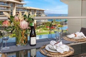 Mesa dispuesta para comer, con una botella de vino, un florero y vista a un hotel y al océano.