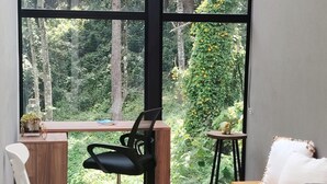 Een kamer met een groot raam, een bureau, een stoel, een bank en een klein tafeltje.