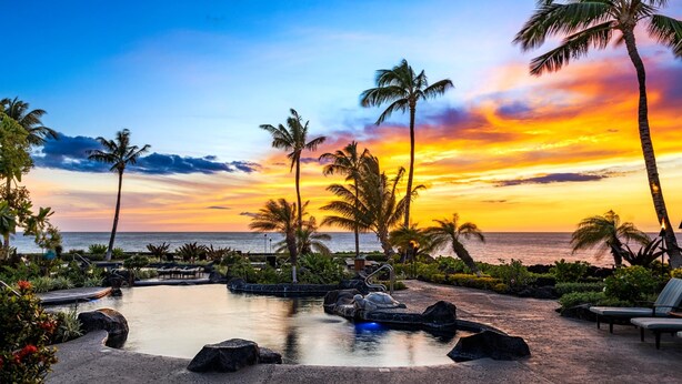 A resort with a swimming pool, lounge chairs, and palm trees. - Halii Kai | Ocean View 7 BR, Sleeps 20 | Car Incl. w/ 6+ Nights | HLI ML-3872 by KBM (Waikoloa)