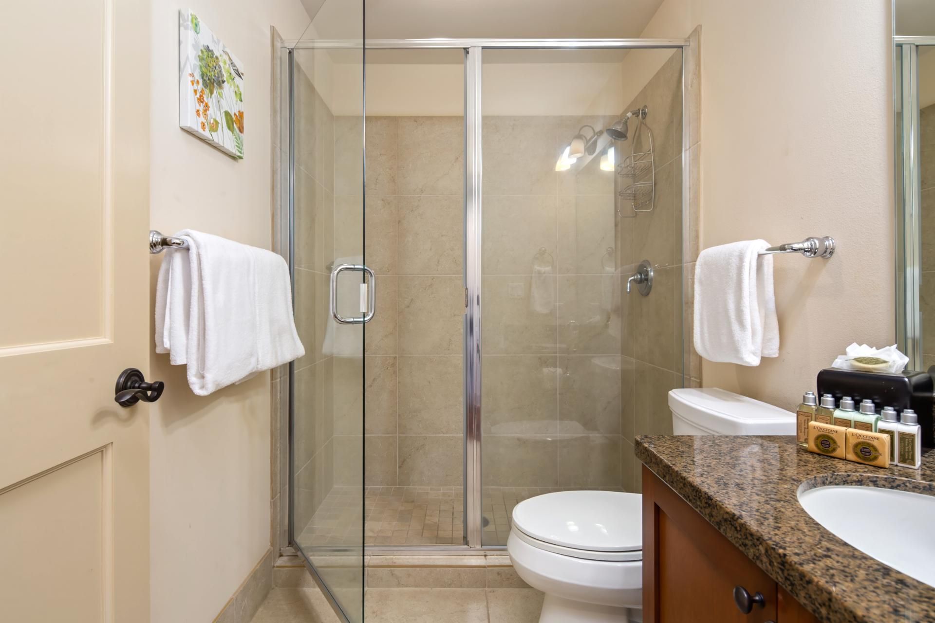 A modern bathroom with a glass-enclosed shower, a toilet, and a sink with toiletries.