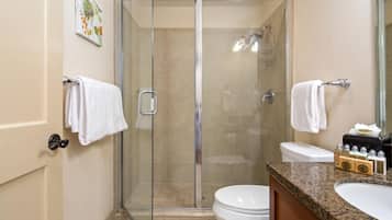 A modern bathroom with a glass-enclosed shower, a toilet, and a sink with toiletries.