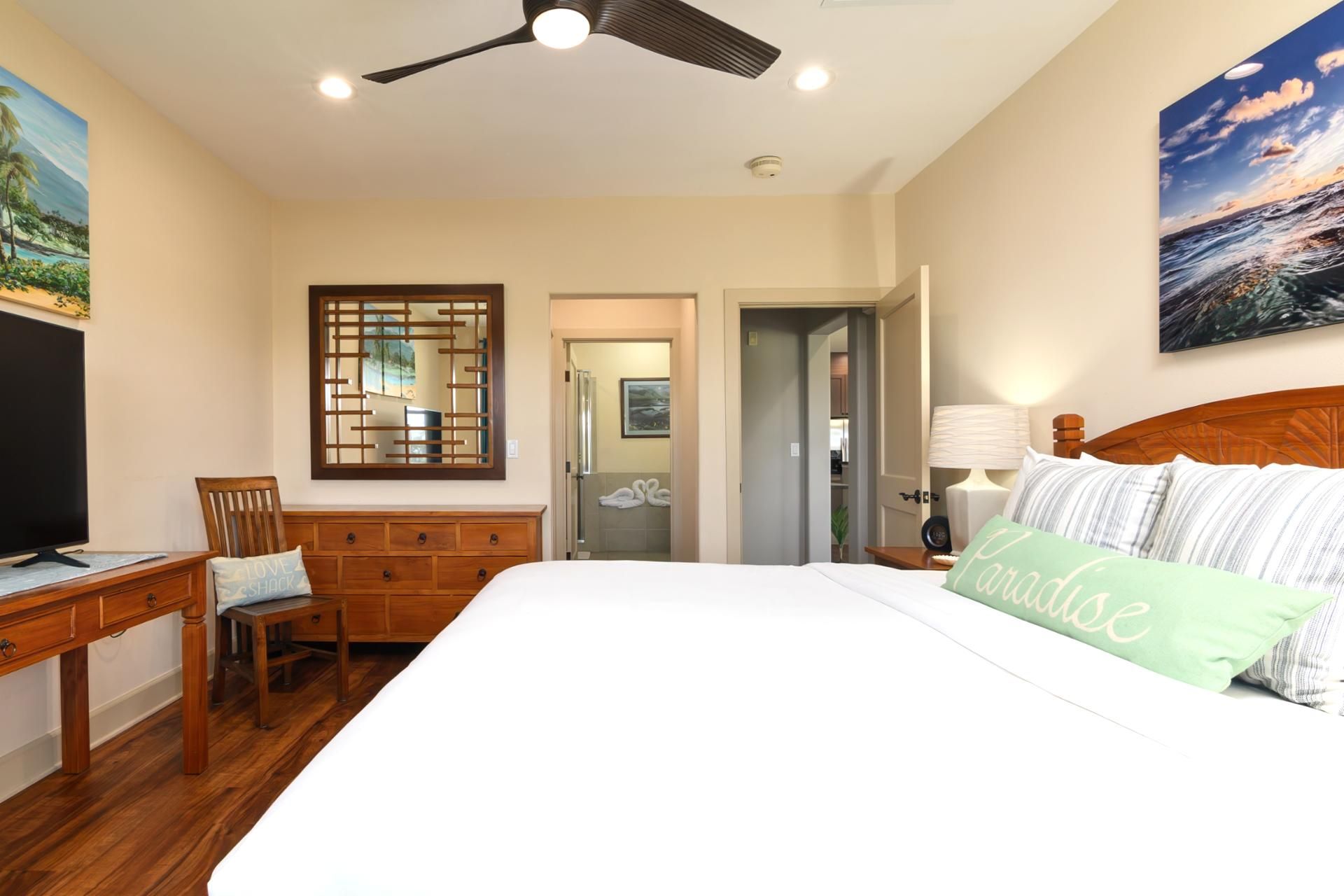 A bedroom with a bed, a desk, a chair, a ceiling fan, and a painting on the wall.