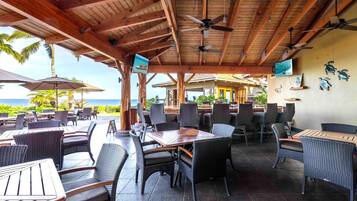 An outdoor dining area with wicker furniture and ceiling fans, overlooking the ocean.