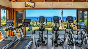 A gym with treadmills and elliptical machines, overlooking a scenic view of the ocean.