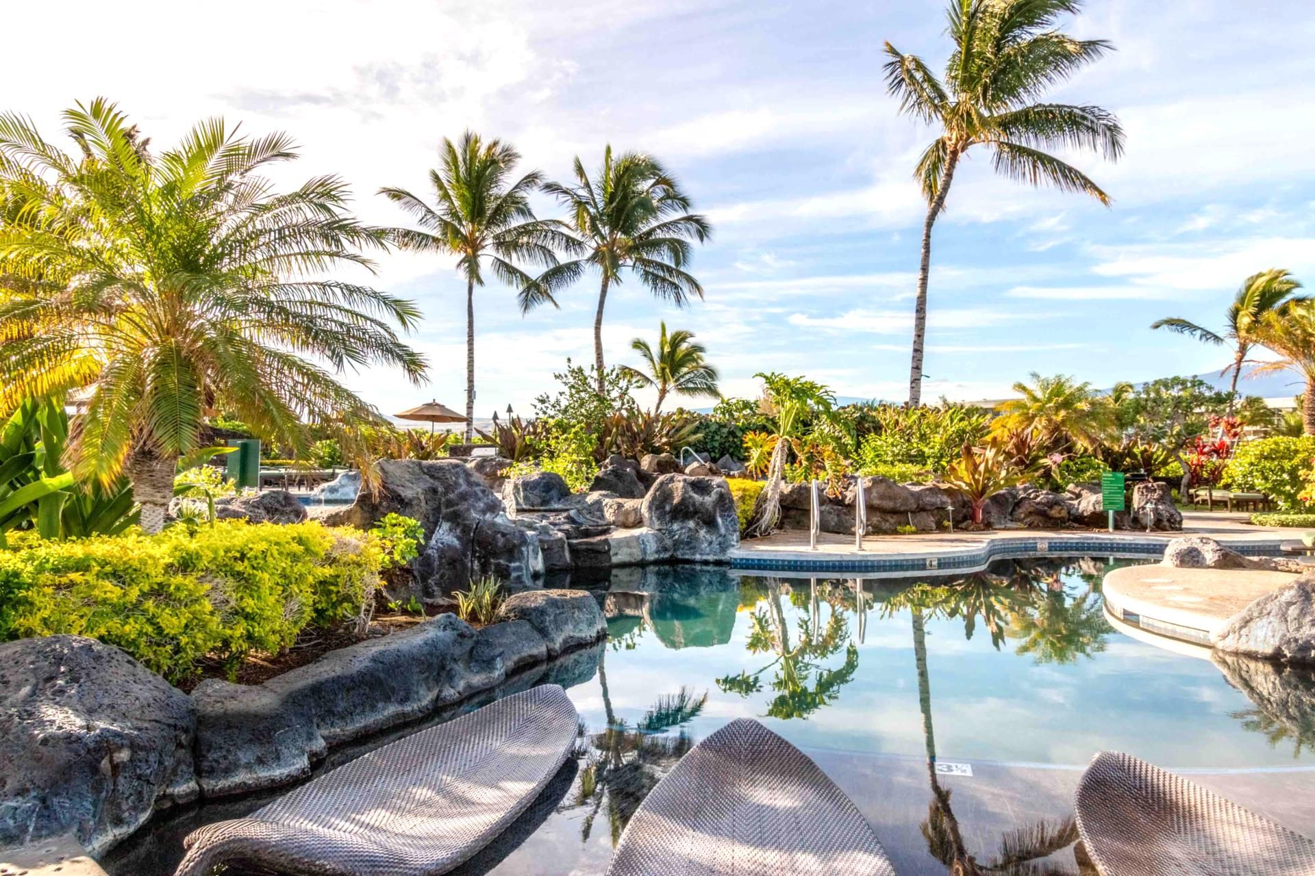A pool area with lounge chairs, palm trees, and a waterfall.