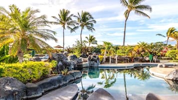A pool area with lounge chairs, palm trees, and a waterfall.