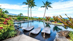 Ein Pool mit Liegestühlen, Palmen und Blick auf den Ozean.
