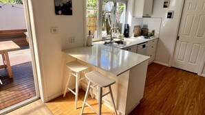 A modern kitchen with a large island, wooden flooring, and a sliding glass door leading to an outdoor area. - Peaceful Family Home in Brookvale for mid-term rental (Brookvale)