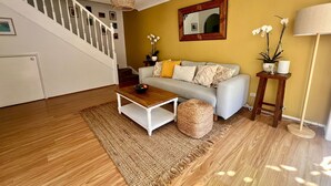 A living room with a staircase, a sofa, a coffee table, a lamp, and a mirror. - Peaceful Family Home in Brookvale for mid-term rental (Brookvale)