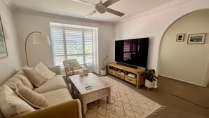A living room with a sofa, coffee table, TV, and a ceiling fan. - Peaceful Family Home in Brookvale for mid-term rental (Brookvale)