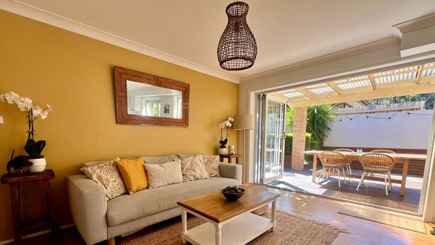 A living room with a sofa, coffee table, and a large window. - Peaceful Family Home in Brookvale for mid-term rental (Brookvale)
