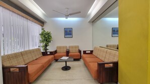A room with a sofa set, a ceiling fan, and two framed pictures on the wall. - Hotel Skylon By Bizzgrow Hotels (Ahmedabad)