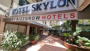 A hotel entrance with a sign for 'Hotel Skylon' by BizzGrow Hotels, surrounded by potted plants and a paved walkway. - Hotel Skylon By Bizzgrow Hotels (Ahmedabad)