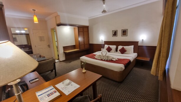 A hotel room with a bed, a desk, a chair, a lamp, a wall-mounted air conditioner, and a ceiling fan. - Hotel Skylon By Bizzgrow Hotels (Ahmedabad)
