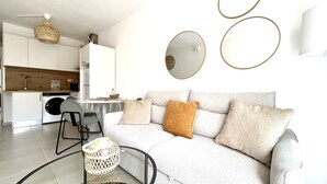 A modern living room with a sofa, a dining table, and a kitchen area in the background. - Welooveyou Coral your place to discover the island (Costa Calma (incl. Urbanización Cañada del Río))