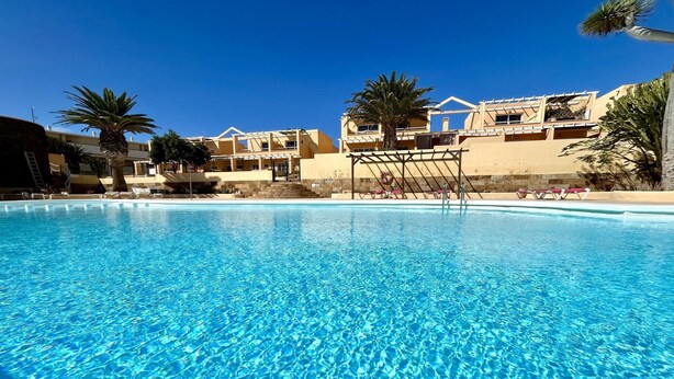A clear blue pool with lounge chairs and palm trees, surrounded by buildings with balconies. - Welooveyou Coral your place to discover the island (Costa Calma (incl. Urbanización Cañada del Río))