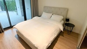 A bedroom with a large bed, a nightstand, and a view through a glass door. - Luxury 2BR 2B Docklands Bright & Modern Apt - Free Covered Parking, 2p sofa bed (Docklands)