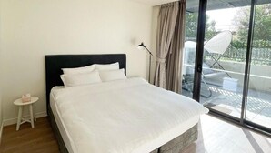 A modern bedroom with a large bed, a small bedside table, a chair, and a view of the outdoors through a glass door. - Luxury 2BR 2B Docklands Bright & Modern Apt - Free Covered Parking, 2p sofa bed (Docklands)
