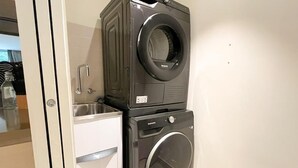 A stacked washer and dryer unit in a room with a white door and a stainless steel sink. - Luxury 2BR 2B Docklands Bright & Modern Apt - Free Covered Parking, 2p sofa bed (Docklands)