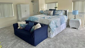 A bedroom with a bed, a ceiling fan, a bedside table with a lamp, a wardrobe, and a small seating area.