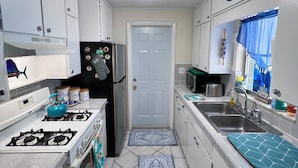 A compact kitchen with white cabinets, a gas stove, a refrigerator, and a microwave.