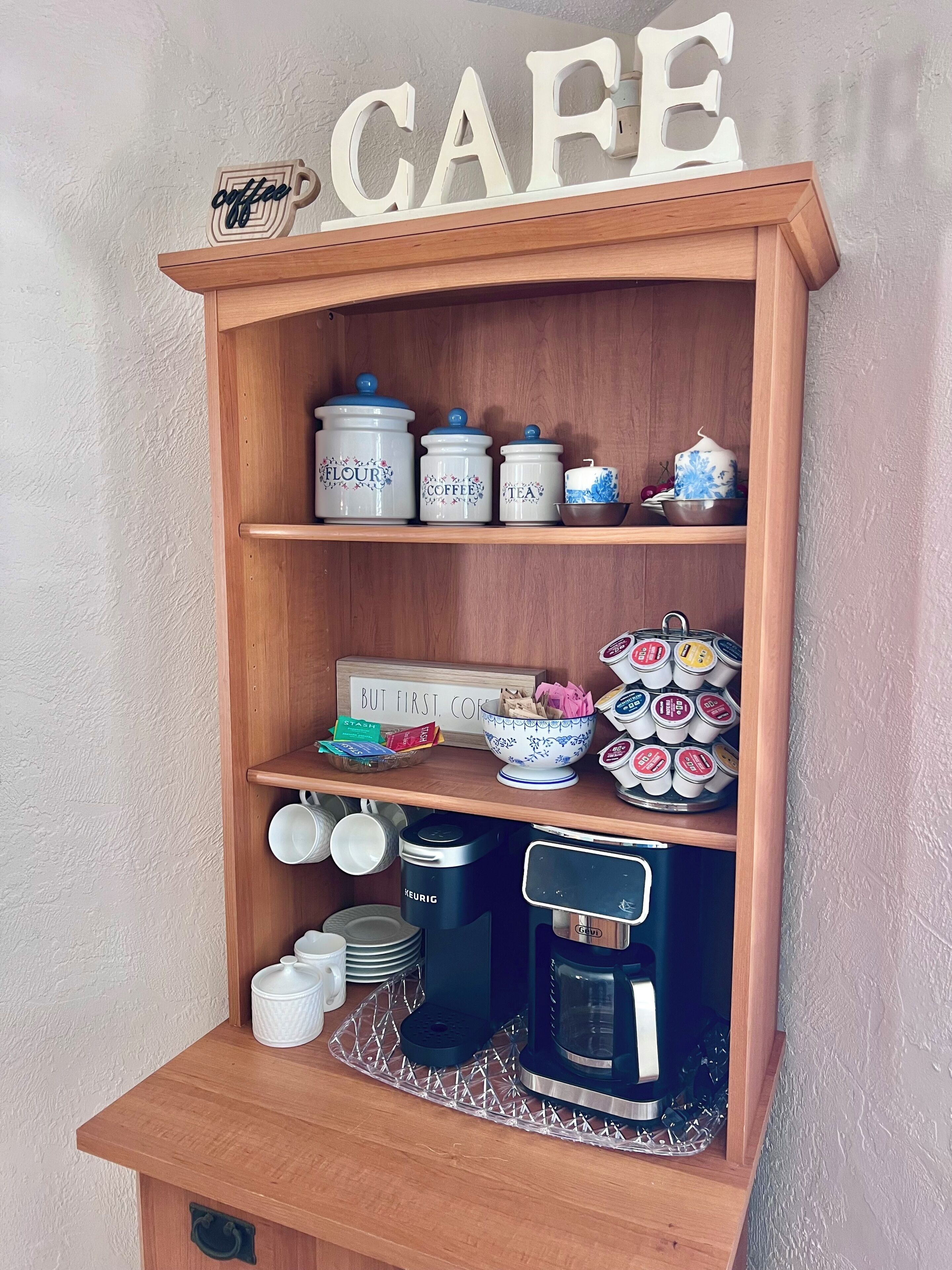 A wooden shelf with labeled containers for flour, coffee, and tea, a coffee maker, and a sign that says 'CAFE'.