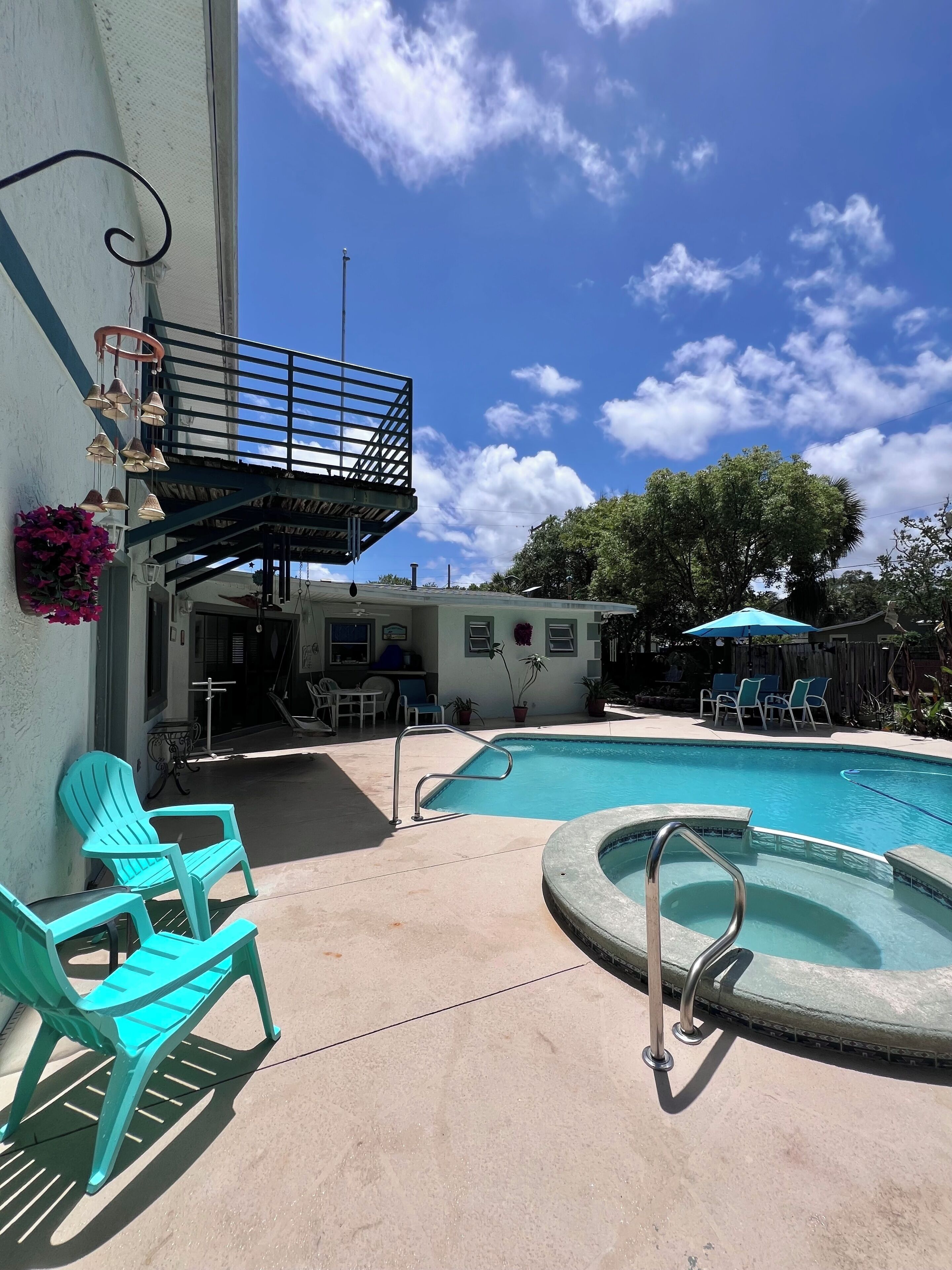 A pool area with chairs, a hot tub, and a balcony with a railing.