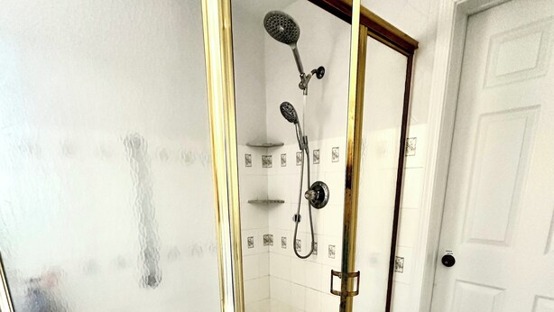 A walk-in shower with a glass door and a gold frame, a showerhead, and a tiled floor. - SEPTEMBER SPECIAL!! Tropical Riverside Oasis with Private Pool •  (Edgewater)