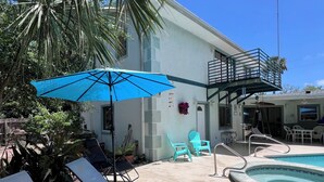 A pool area with lounge chairs, a blue umbrella, and a building with a balcony. - SEPTEMBER SPECIAL!! Tropical Riverside Oasis with Private Pool •  (Edgewater)