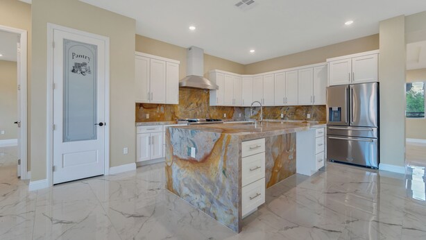 A modern kitchen with marble countertops, stainless steel appliances, and white cabinetry.