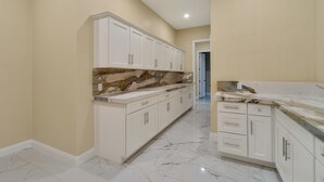 A kitchen with white cabinets, a marble countertop, and a stone backsplash.
