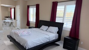 A modern bedroom with a curved bed, two bedside tables, a large window with curtains, and a bathroom with a bathtub and mirror.