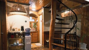 A wooden interior with a spiral staircase, a kitchen area with a water dispenser, and a shelf with jars. - Blueridge Mountain Cabin (Baguio)