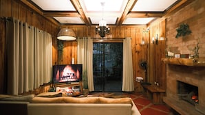 A cozy living room with wooden walls, a fireplace, a television, and a large window. - Blueridge Mountain Cabin (Baguio)