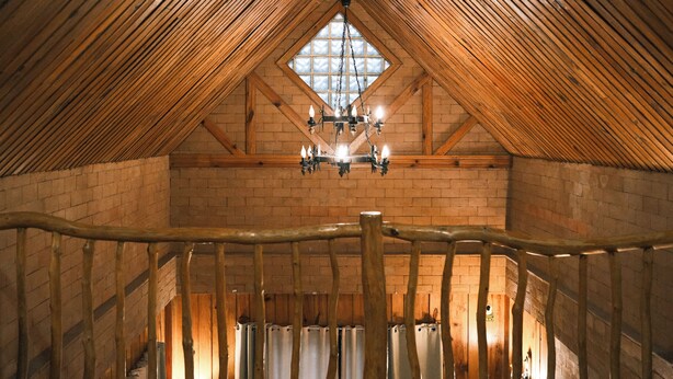A high-ceilinged attic room with exposed wooden beams, a central chandelier, and a brick wall. - Blueridge Mountain Cabin (Baguio)