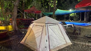 Een tent op een grindpad, met bomen en een rode constructie op de achtergrond.