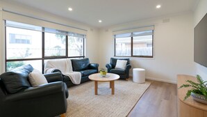 A modern living room with a sectional sofa, a small round table, and a potted plant. - Light filled 2 bedroom central retreat (Torquay)