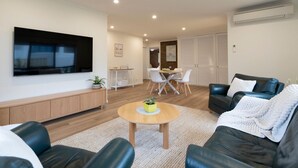 A modern living room with a flat-screen TV, a wooden cabinet, a round coffee table, and a black leather sofa. - Light filled 2 bedroom central retreat (Torquay)