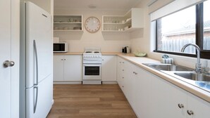 A kitchen with white cabinets, a stove, a microwave, and a sink. - Light filled 2 bedroom central retreat (Torquay)