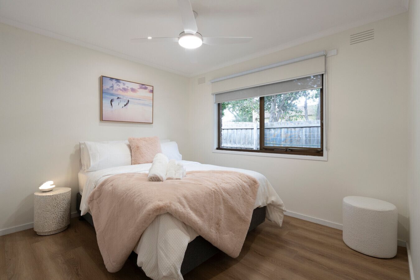 A bedroom with a bed, a bedside lamp, a window, and a ceiling fan.