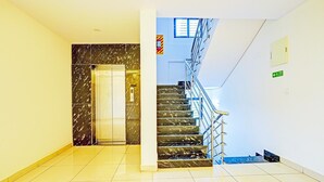 A hotel lobby with a marble elevator, a staircase with metal railings, and a fire exit sign. - Deluxerenigunta Near Railway Station (Bengaluru)