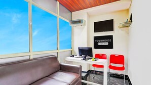A room with a leather sofa, a desk with a computer, two red chairs, a TV, and a sign that reads 'TOWNHOUSE Company-Serviced.' - Deluxerenigunta Near Railway Station (Bengaluru)