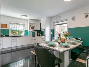 A modern kitchen with white cabinets, a dining table set with green plates, and a view of greenery outside. - Spacious vacation home where your dog is welcome (Radfeld)