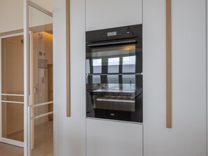 A modern kitchen with a built-in oven and microwave, a wooden door frame, and a glass partition. - Beautiful 2-bedroom apartment with ocean views (Middelkerke)