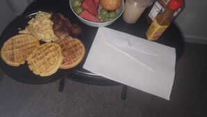 A breakfast plate with waffles, scrambled eggs, bacon, a bowl of fruit, a glass of milk, and a bottle of syrup. - Saffire Villa  (Tacoma)