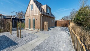 Een modern huis met een schuin dak, een grindpad en een houten hek.
