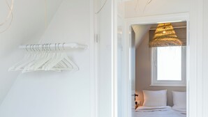Een slaapkamer met een bed, een hanglamp en een witte muur met een kledingrek.