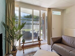 Ein Wohnzimmer mit einer Couch, einer Pflanze, einem Holztisch und einer Glasschiebetür, die zu einem Außenbereich führt.