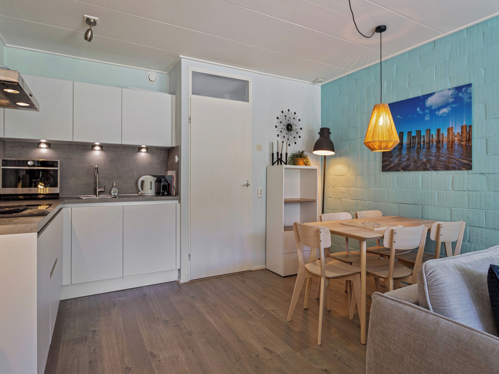 A compact kitchen with white cabinets, a built-in oven, and a dining area with a wooden table and chairs.