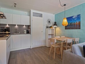 Eine kleine Küche mit weißen Schränken, einem Einbauofen und einem Essbereich mit Holztisch und Stühlen.